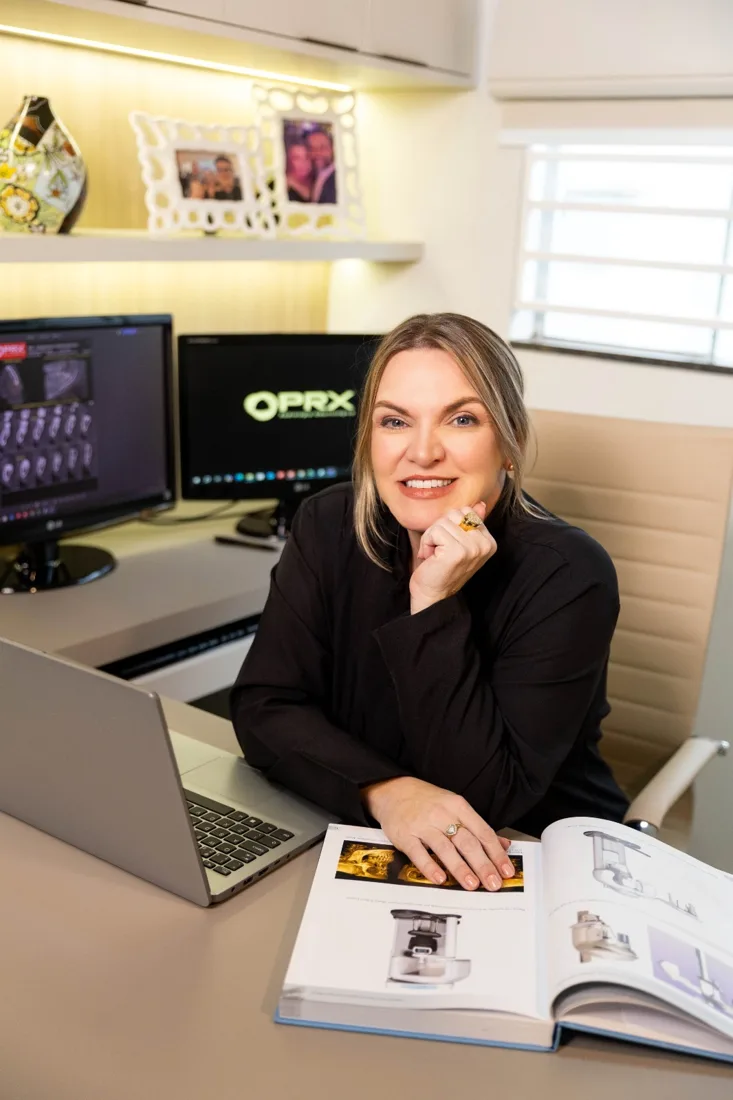 Dra. Fabiana Fernandes Segato na mesa de trabalho da PRX, com os monitores de imagem ao fundo
